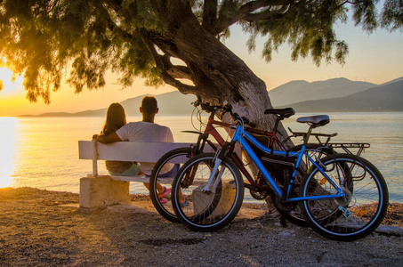 一对情侣看日落坐在海边的长椅上