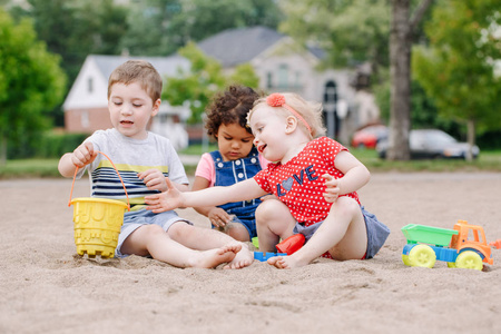 三可爱的白种人和拉美裔儿童的肖像, 孩子们坐在沙盒里玩塑料五颜六色的玩具。小女孩和男孩朋友一起在操场上玩得开心