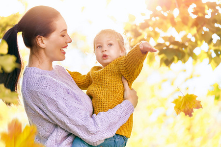 在秋天走上幸福的家庭 母亲和女儿在公园散步，享受美丽的秋天大自然