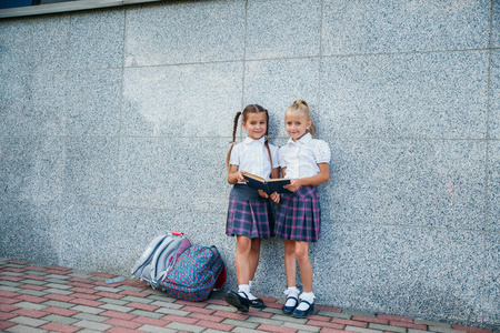 小学生的小学。女孩有背包和书籍在户外建筑附近。课程开始。秋天的第一天