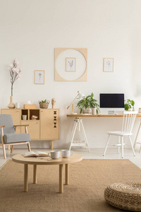 木桌和脚凳在褐色地毯在白色工作区内部与海报和扶手椅。真实照片