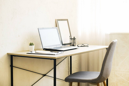 笔记本电脑, 剪贴板, 仙人掌家庭植物, 供应和折叠眼镜在木桌上, 灰色的椅子在办公室里充满阳光。设计师创造性的工作空间概念。关