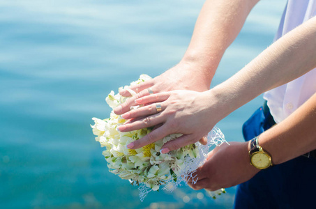 特写新娘和新郎的手与结婚戒指和花束。爱情和婚姻。在河的背景婚礼配件和装饰