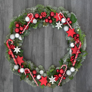 圣诞和冬季花圈与糖果手杖和摆设装饰品, 冬青, 槲寄生, 常春藤和云杉冷杉在质朴的灰色木材背景