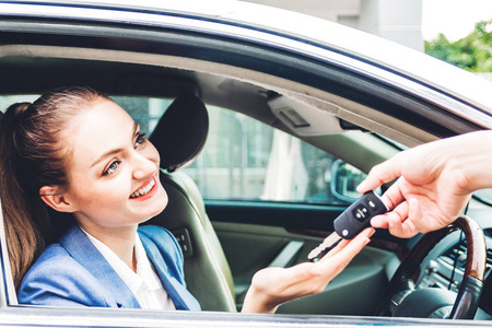 销售经销商给新车的车钥匙与商界妇女坐在车上微笑. 租车概念