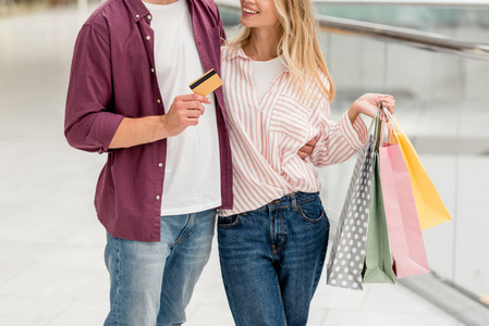 男子显示信用卡的部分视图而他的女朋友站在购物中心附近的购物袋