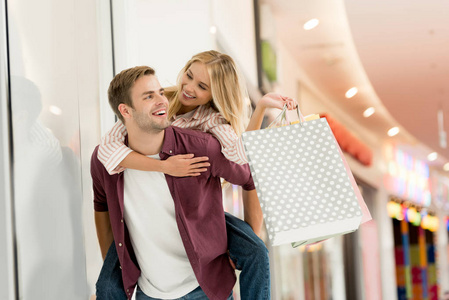 年轻男子背着背包骑着购物袋在购物中心的女朋友