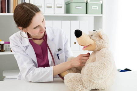 在白大衣美丽微笑的女医生检查玩具熊
