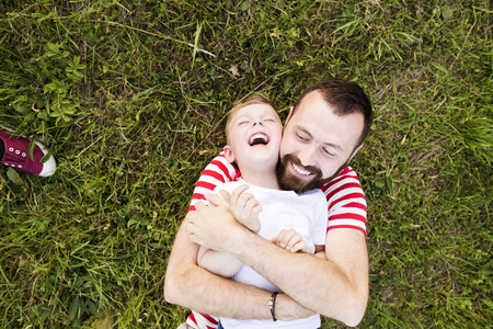 时髦的父亲和小儿子躺在绿色的草地上。夏季的一天