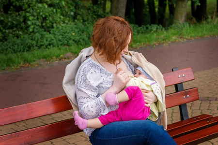 母亲母乳喂养婴儿在公园的长凳上