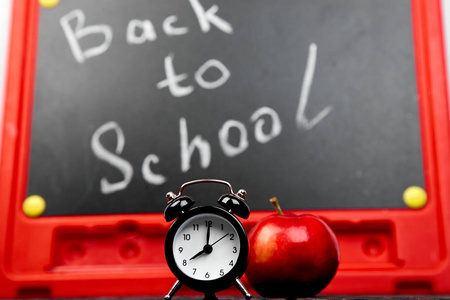 回到学校的文字在黑板上用粉笔与红苹果和闹钟附近的黑板背景。静物