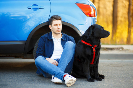 英俊的男子穿着时髦的衣服, 狗坐在车旁。享受旅游