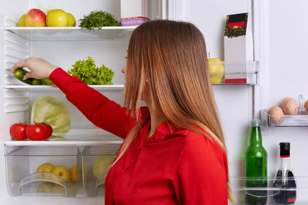 室内拍摄的年轻女性用长直的黑发, 把蔬菜放在冰箱的架子上, 只吃健康的食物。在厨房的女人。主妇要做蔬菜沙拉。营养