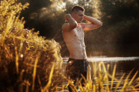 一个年轻人站在河边, 在日落时洗脸。一个裸露躯干的在水里