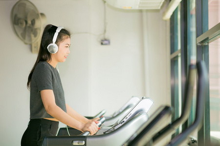 亚洲美女的健身房和听音乐在跑步机上