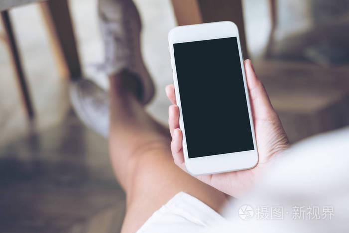 现代木地板背景下手持白色手机的女性手持手机样机图像