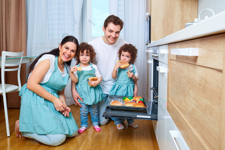 双胞胎女孩和她的父母在厨房里吃包子。一种幸福