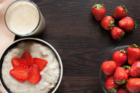 热的燕麦粥，鱼片的草莓和温暖可可带着在一张木桌上的牛奶