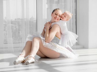 年轻母亲拥抱小微笑的女儿在芭蕾演播室