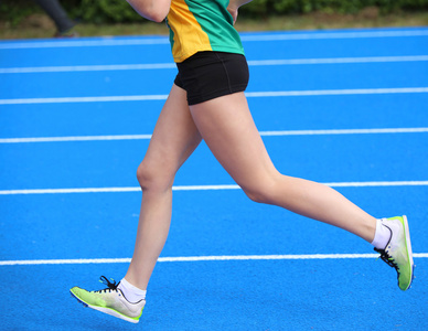年轻的女运动员腿跑在田径跑道