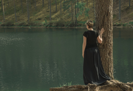 孤独的年轻女子中长裙子站在岸边的湖，看起来到距离
