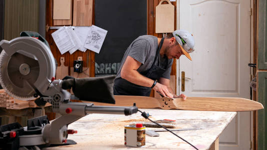 有经验的木匠在工作衣物和小付多少营业税所有者在木工车间工作, 用砂纸抛光儿童直升机刀片在车间工作台