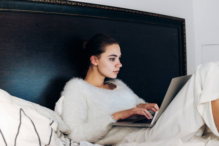 年轻美丽的自由职业者女孩工作努力, 坐在床上与笔记本电脑