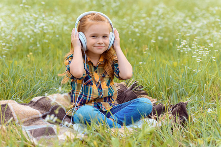 可爱的孩子听音乐的耳机, 而坐在毯子在野外与野花