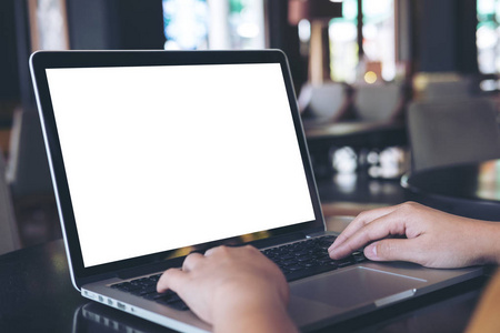 女子用空白的白色屏幕，在现代咖啡厅的木桌上的笔记本电脑样机形象