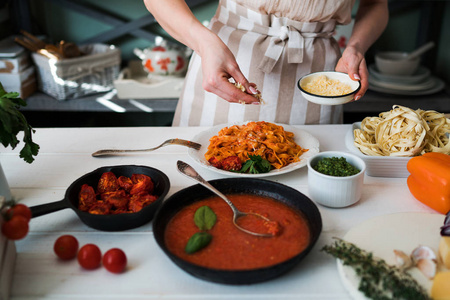食物, 家庭和人的概念。在家里做饭的女人做自制面食。配有配料的面食。在白色木质背景下的西红柿, 大蒜, 欧芹, 胡椒和干酪