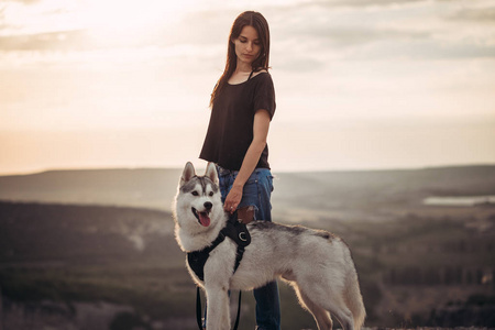 美丽的女孩玩与狗 灰色和白色赫斯基 在山上日落
