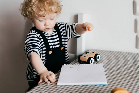 孩子衣服上的开朗金发男孩在厨房的桌子上画了一个白色的笔记本。