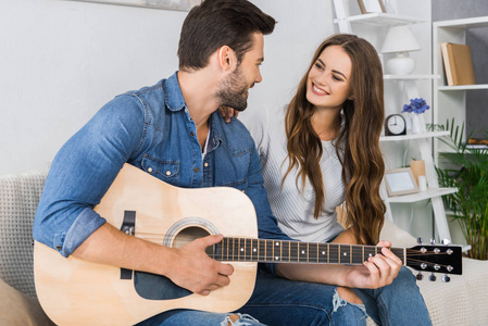 微笑夫妇与声学吉他看对方在家里的沙发上