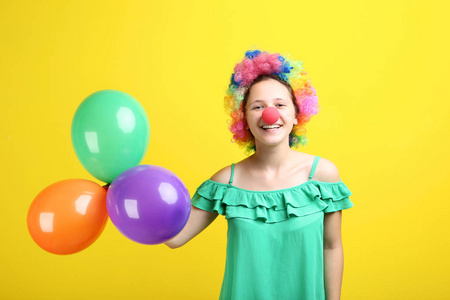 黄色背景的小丑假发和气球的年轻女孩