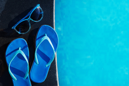 蓝色拖鞋和太阳眼镜附近游泳池假日概念