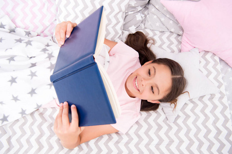女孩躺在床上看书的最高视图。鼓励有用的习惯。孩子准备上床睡觉。在舒适的卧室愉快的时间。小女孩长头发可爱的睡衣放松和看书。满意与幸