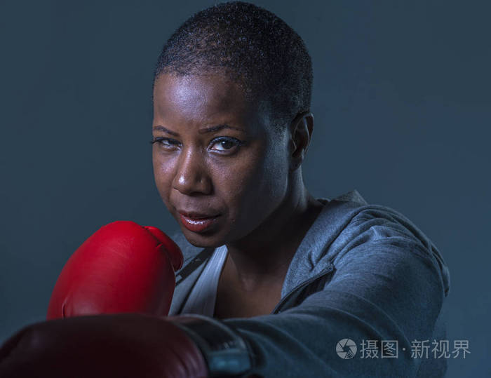 关闭脸上的年轻愤怒和挑衅黑人美国运动妇女在拳击手套训练和假扮成一