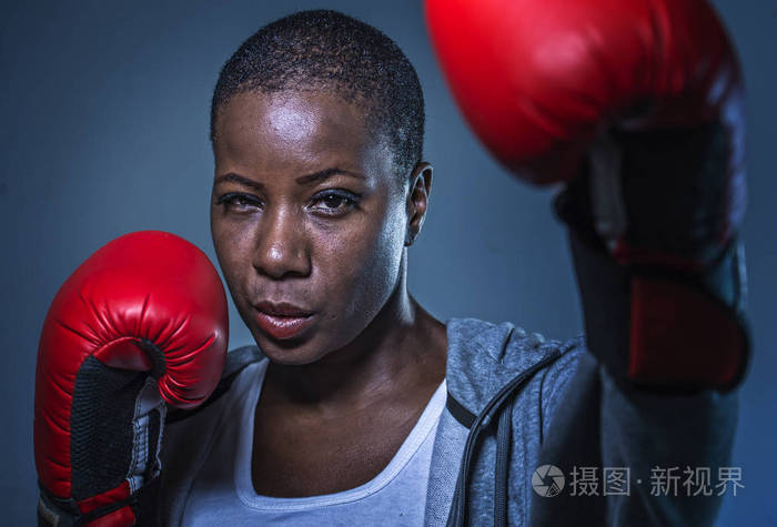 关闭脸上的年轻愤怒和挑衅黑人美国运动妇女在拳击手套训练和假扮成一