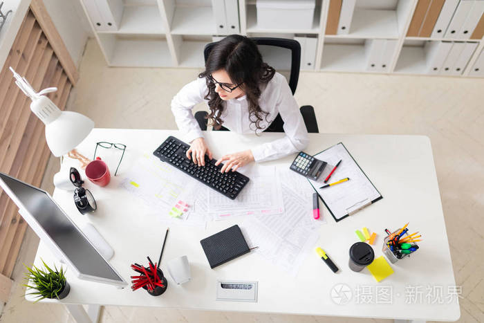 一个年轻的女孩坐在办公室里的电脑和工作的文件