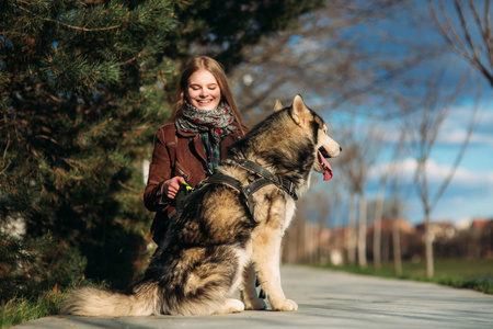 一个微笑的女孩沿着河堤走着一条狗。美丽的沙哑的狗