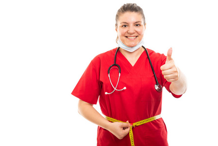 身穿红色磨砂的年轻医护护士肖像用 copyspace 广告区测量腰部显示拇指的白色背景