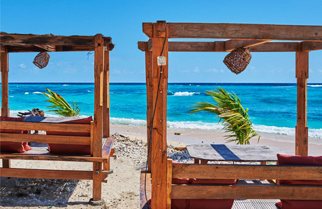 热带度假村的浪漫露台休息室。在一个美丽的海滩上的空木休息室床在一个闪亮的绿松石海洋的背景。夏天的早晨。在美丽的海滩上放松私人日光