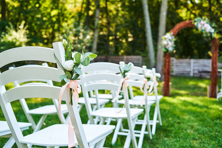 在拱门 outroods 两侧的婚礼椅上的白色鲜花与粉红色丝带复制空间。在花园里的草坪上为客人准备的木制椅子婚礼仪式