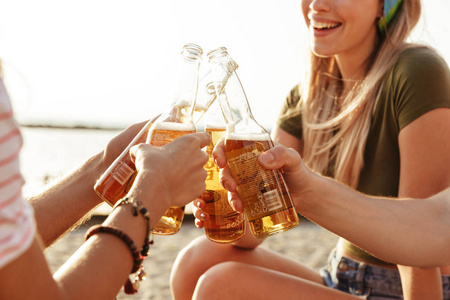 一群兴高采烈的朋友身着夏日服装, 在海滩上用啤酒瓶敬酒。