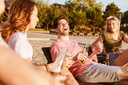 一群开朗的朋友穿着夏天的衣服喝啤酒, 而在海滩放松