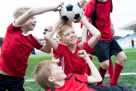 少年足球队的肖像在户外体育场赢得比赛后高兴地一起捧着球和欢呼, 集中在红头发队队长在中心