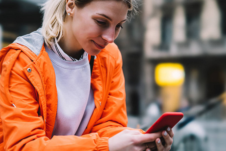 在城市街道上, 使用手机数据互联网连接关闭年轻女性的视线。白种时髦女孩橙色夹克阅读短信通过聊天应用智能手机