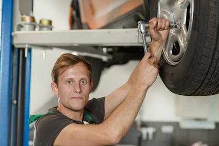 一个年轻英俊的机修工正试图在汽车车间为轮胎服务扭开汽车车轮。
