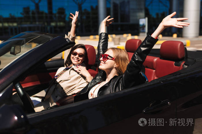 两个开朗的女孩快乐地花时间一起驾驶敞篷车在城市街道室外