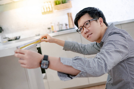 年轻的亚洲人使用卷尺测量在陈列室的现代厨房柜台上的层压台面。家居装修家具。室内设计理念